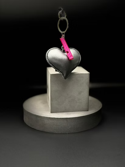 Heart-shaped keychain with a pink tag on a gray pedestal against a black background
