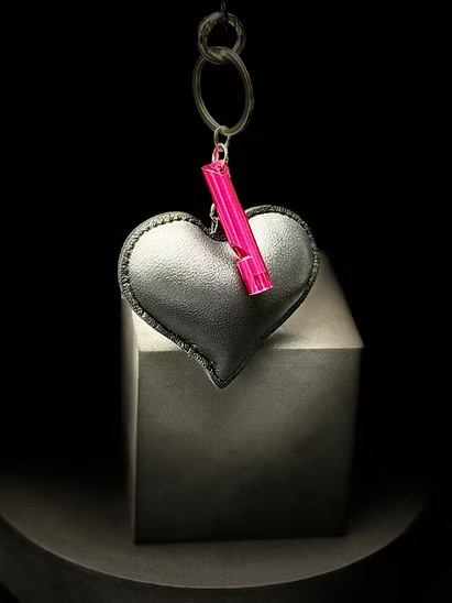 Heart-shaped keychain with a pink clip on a metallic stand against a black background