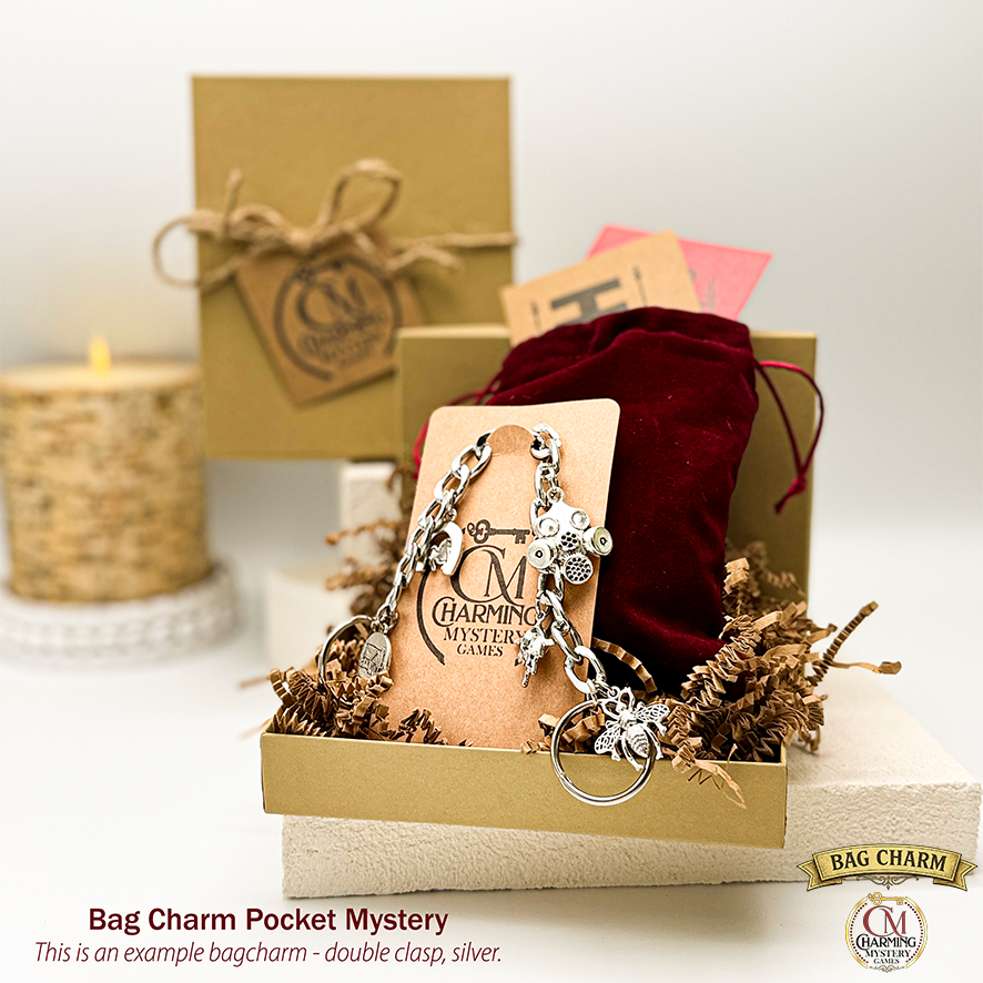 A bag charm hanging on a card in front of a velveteen pouch. In the background is a kraft jewelry box and a candle. 