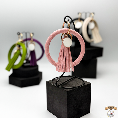 Pink tassel keychain on a black stand with blurred earrings in the background