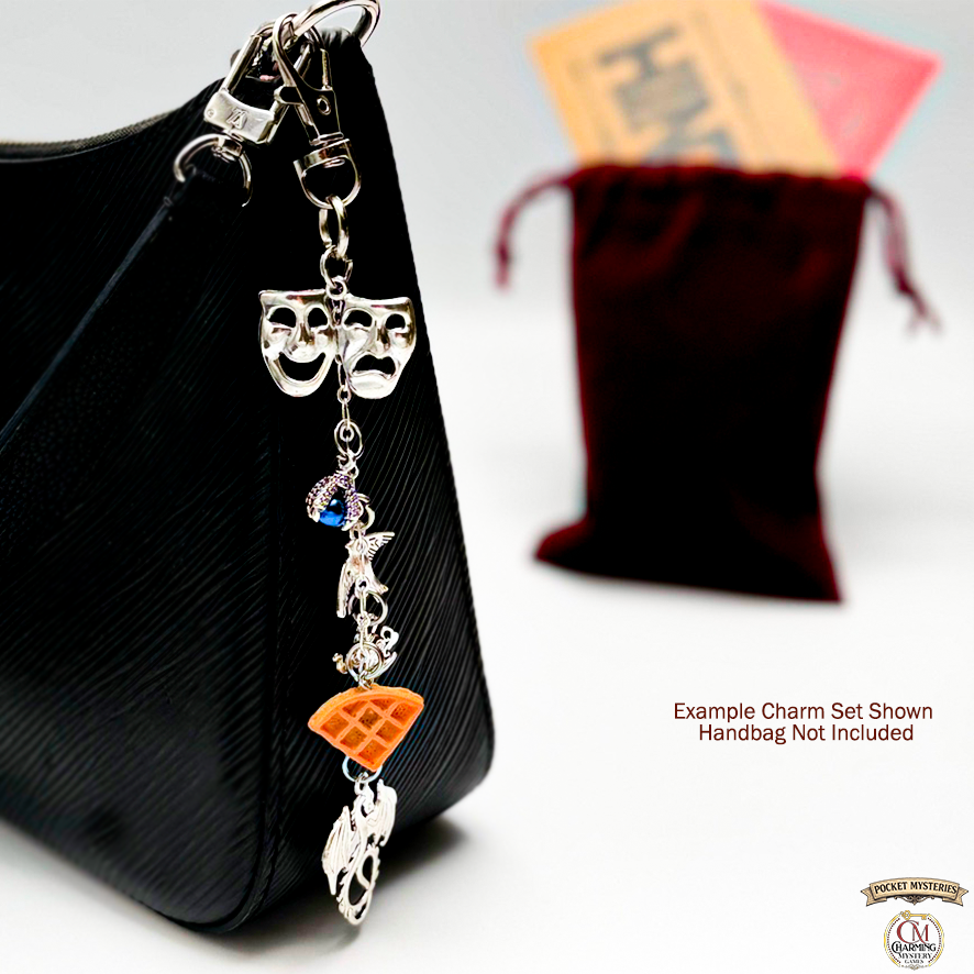 Charm set with theater masks and other charms on a black handbag with a red pouch in the background.