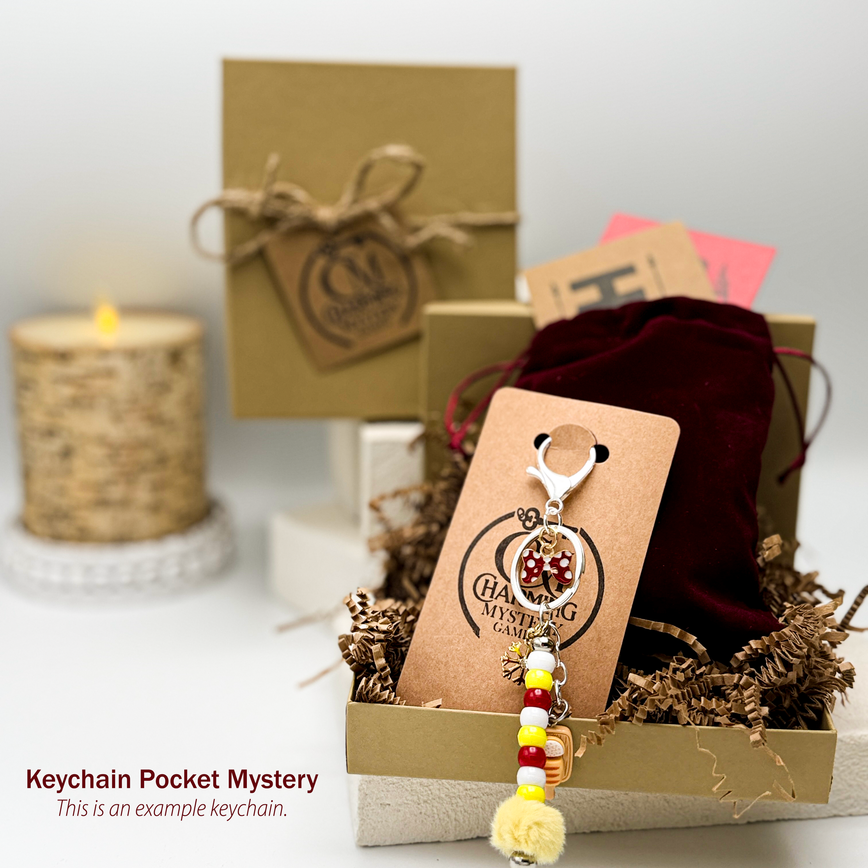 A cute red and yellow keychain is on a card in front of a velveteen bag with a kraft jewelry box in the background.