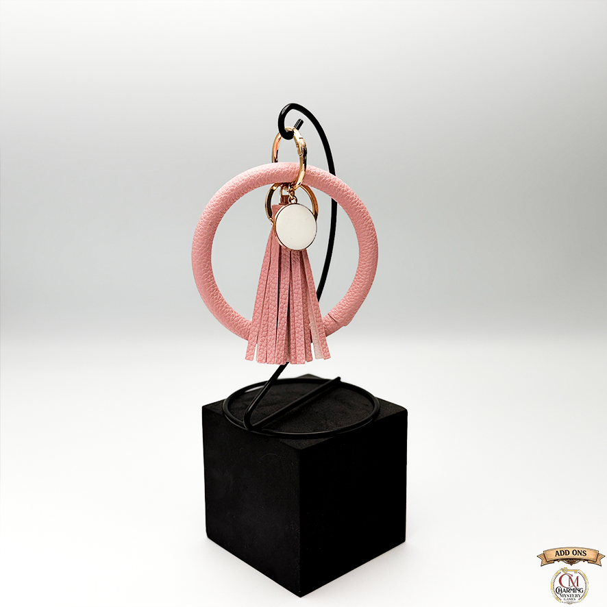 Pink tassel keychain on a black cube with a white background