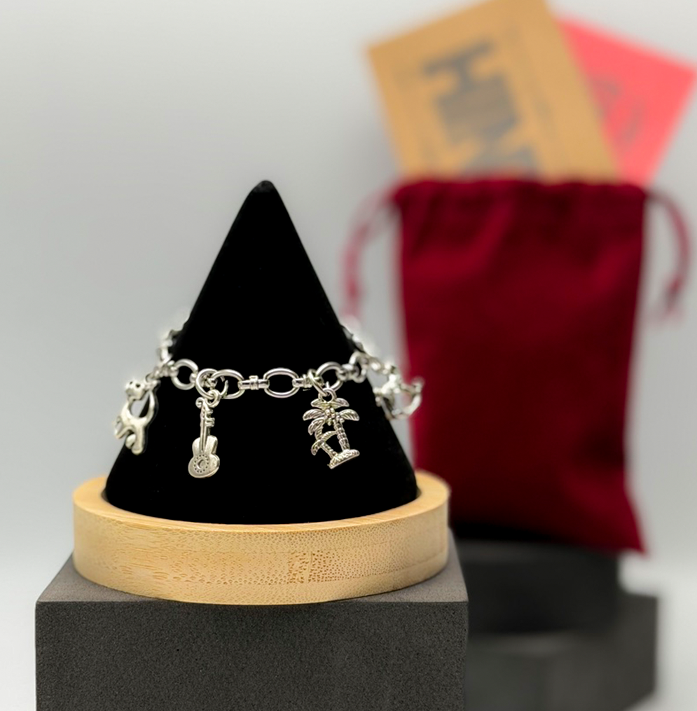 Bracelet with charms on a black cone-shaped stand with a blurred red bag in the background