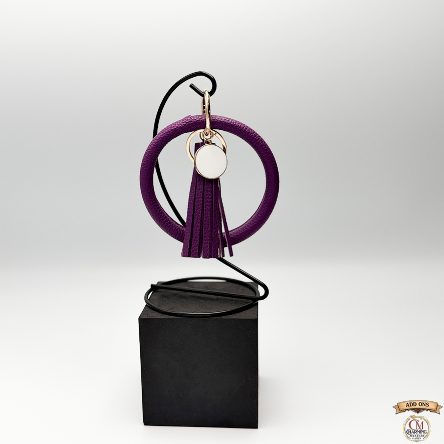 Purple circular keychain with tassel on a black stand against a white background